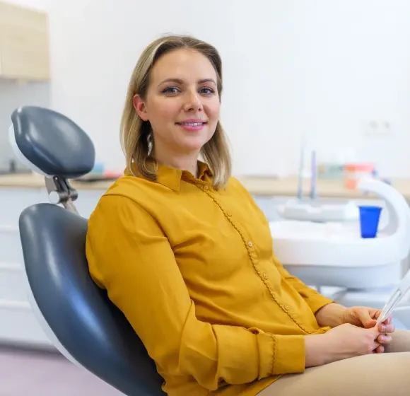 Woman in yellow shirt sitting in dental chair during cleaning and exam appointment.