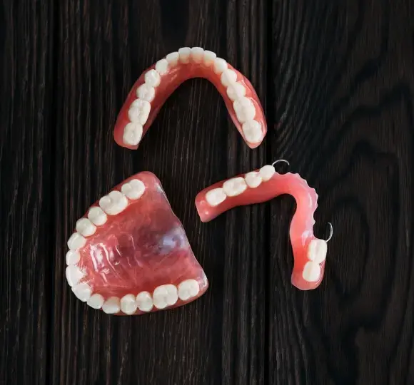Three custom dentures and partial dentures displayed on dark wood background.