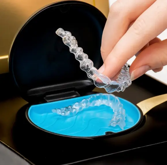 Clear Invisalign aligner being held above blue storage case by dental patient.