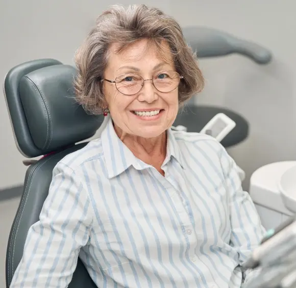 Smiling female dentist in light blue striped shirt seated in dental office chair.