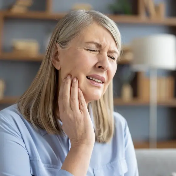 Woman holding her cheek in pain, experiencing TMJ discomfort or dental pain.
