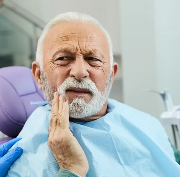 Senior man experiencing tooth pain in dental office chair.